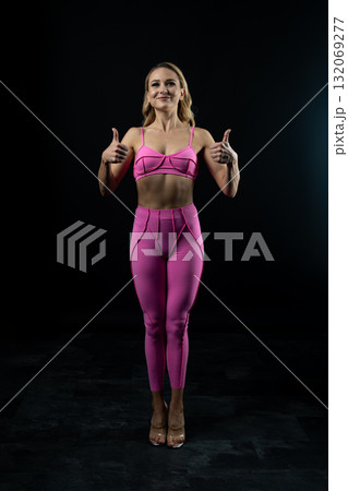 Confident fitness model posing in pink sportswear on black background Confident fitness model posing in pink sportswear on black background 132069277