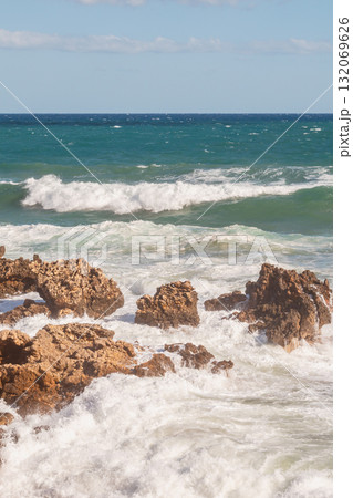 Sea foam crashing against rocky shore. 132069626