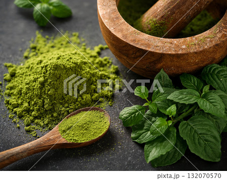 Wooden mortar and pestle with green herbal powder. Concept of traditional herbal medicine, natural remedies, or Ayurvedic preparation with fresh leaves on a dark stone background. Wooden mortar and pestle with green herbal powder. Concept of traditional herbal medicine, natural remedies, or Ayurvedic preparation with fresh leaves on a dark stone background. 132070570