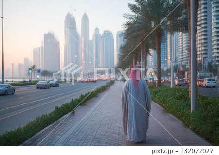 Arab man walking along a city sidewalk with modern skyscrapers and palm trees in the background Arab man walking along a city sidewalk with modern skyscrapers and palm trees in the background 132072027