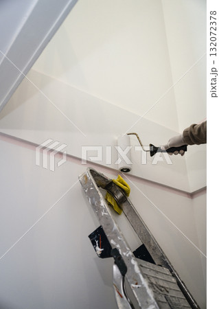 A close-up of a hand in a protective glove painting a light-colored wall with a roller A close-up of a hand in a protective glove painting a light-colored wall with a roller 132072378