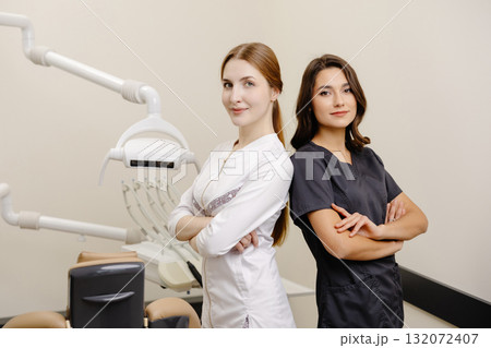 Smiling dentist and assistant with crossed hands looking at the camera in dental clinic Smiling dentist and assistant with crossed hands looking at the camera in dental clinic 132072407