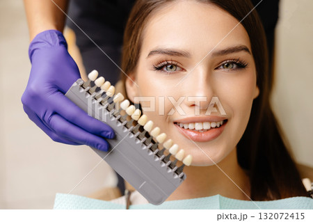 Dentist choosing teeth enamel shade color for young smiling female patient before whitening procedure Dentist choosing teeth enamel shade color for young smiling female patient before whitening procedure 132072415