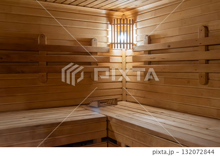 Empty wooden sauna interior with tiered benches and warm light Empty wooden sauna interior with tiered benches and warm light 132072844
