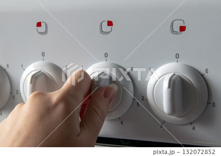 Hand turning stove knob to adjust cooking temperature on kitchen oven 132072852