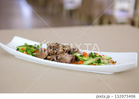 Serving of sliced boiled beef tongue with pickled cucumbers and bell peppers drizzled with olive oil soy sauce and crushed garlic topped with black and white sesame and microgreens on white plate. Serving of sliced boiled beef tongue with pickled cucumbers and bell peppers drizzled with olive oil soy sauce and crushed garlic topped with black and white sesame and microgreens on white plate. 132073406
