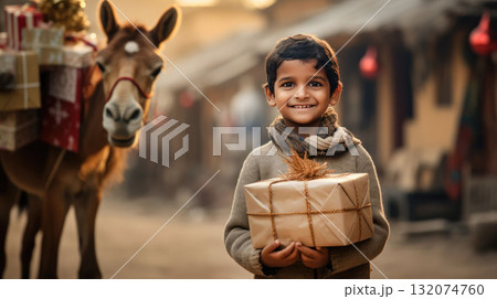 Indian kid with big giftbox is looking to the camera dusty street on background. Christmas support. Give and share kindness. Indian kid with big giftbox is looking to the camera dusty street on background. Christmas support. Give and share kindness. 132074760