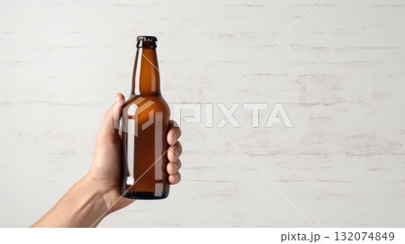 Amber Beer Bottle in Hand Isolated on Whitewashed Brick Wall Background Amber Beer Bottle in Hand Isolated on Whitewashed Brick Wall Background 132074849