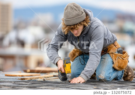 Young male construction worker using power tool on rooftop during project Young male construction worker using power tool on rooftop during project 132075072
