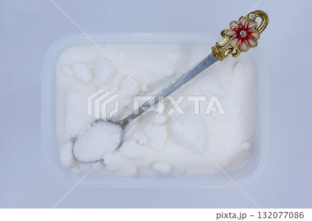 A plastic container filled with sugar with a small spoon 132077086