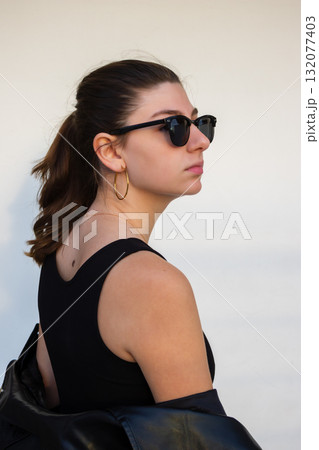 Modern urban portrait of a blonde woman in leather jacket and sunglasses. Light wall background 132077403