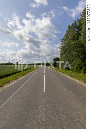 a paved road in rural areas in the summer with cloudy weather and a sky with lots of clouds, a narrow country road covered with asphalt 132077890
