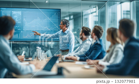 Executive giving a data-driven presentation on a large digital screen to colleagues in a modern office boardroom. Ideal for finance, technology, analytics, corporate strategy, training 132077981