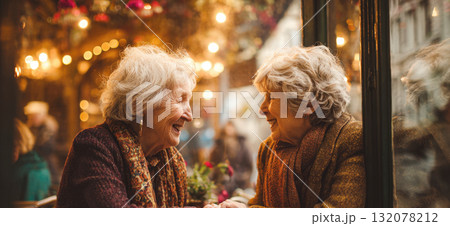 Horizontal portrait of two happy senior women (friends or sisters) laughing together at a cafe window. Captures joy, friendship, aging, connection in a warm, cozy, vintage atmosphere with bokeh lights 132078212