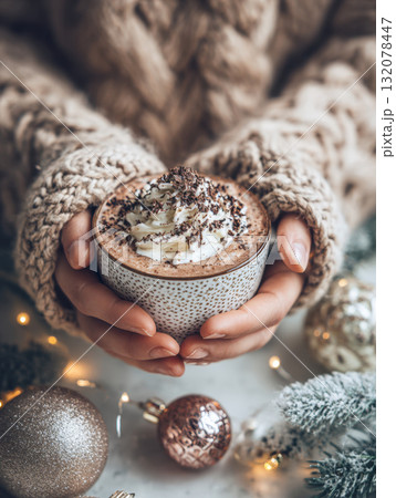 A close-up, vertical shot of hands in a chunky cable knit sweater holding a warm mug of hot chocolate or cocoa garnished with whipped cream and chocolate shavings. 132078447