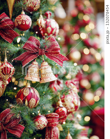 A richly decorated Christmas tree with a vertical focus on luxurious red and gold ornaments, textured ribbon bows, and a pair of golden bells. The background features a beautiful bokeh of warm lights A richly decorated Christmas tree with a vertical focus on luxurious red and gold ornaments, textured ribbon bows, and a pair of golden bells. The background features a beautiful bokeh of warm lights 132078454