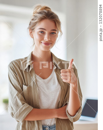 A beautiful, smiling young woman with her hair in a messy bun and wearing casual olive-green overshirt, white t-shirt stands indoors with her arms crossed, giving clear, confident thumbs up to camera A beautiful, smiling young woman with her hair in a messy bun and wearing casual olive-green overshirt, white t-shirt stands indoors with her arms crossed, giving clear, confident thumbs up to camera 132078894