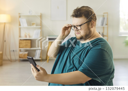 Man adjusting glasses while reading smartphone, seeking focus and clarity at home Man adjusting glasses while reading smartphone, seeking focus and clarity at home 132079445