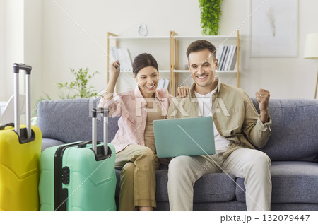 Travel couple with luggage celebrating vacation booking, people sitting on sofa 132079447