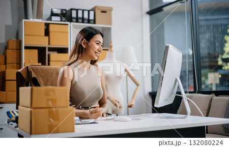 Asian woman prepares parcels and checks online orders on tablet and laptop for delivery online shopping and small business success 132080224