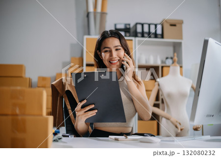 Asian woman prepares parcels and checks online orders on tablet and laptop for delivery online shopping and small business success 132080232