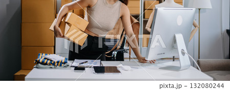 Asian woman prepares parcels and checks online orders on tablet and laptop for delivery online shopping and small business success 132080244