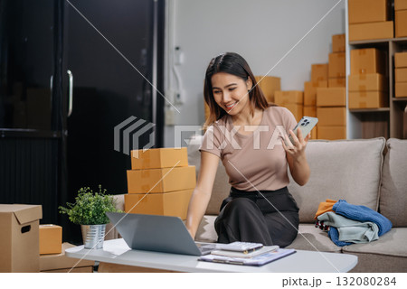 Asian woman prepares parcels and checks online orders on tablet and laptop for delivery online shopping and small business success 132080284