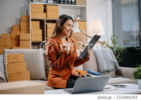 Asian woman prepares parcels and checks online orders on tablet and laptop for delivery online shopping and small business success Asian woman prepares parcels and checks online orders on tablet and laptop for delivery online shopping and small business success 132080293