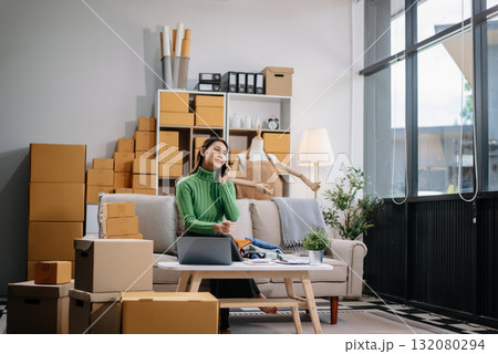Asian woman prepares parcels and checks online orders on tablet and laptop for delivery online shopping and small business success 132080294