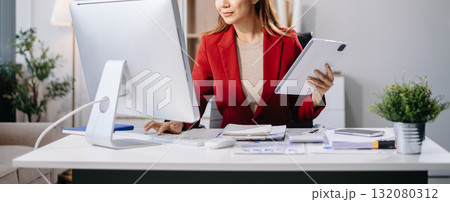 Young beautiful woman typing on tablet and laptop while sitting at the working white table in modern office 132080312