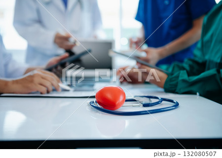 Medical team having a meeting with doctors in white lab coats and surgical scrubs seated at a table discussing a patients working online using computers Medical team having a meeting with doctors in white lab coats and surgical scrubs seated at a table discussing a patients working online using computers 132080507