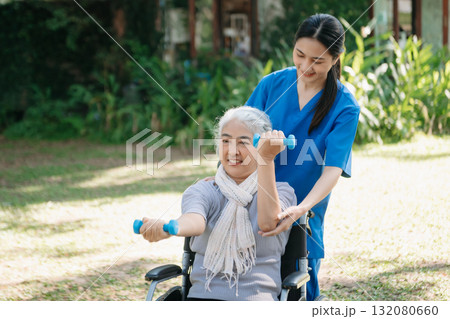 Asian physiotherapist helping elderly woman patient stretching arm during exercise correct with dumbbell in hand during training hand with patient Back problems in the garden. 132080660