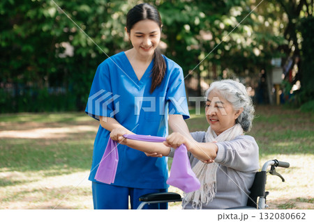 Asian physiotherapist helping elderly woman patient stretching arm during exercise correct with dumbbell in hand during training hand with patient Back problems in the garden. 132080662