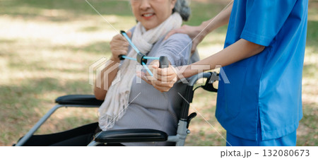 Asian physiotherapist helping elderly woman patient stretching arm during exercise correct with dumbbell in hand during training hand with patient Back problems in the garden. 132080673