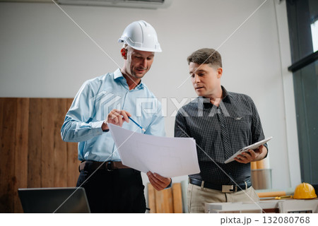 Two colleagues discussing data working and tablet, laptop with architectural project at construction site 132080768