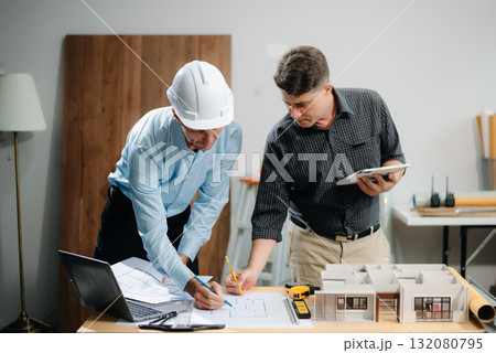 Two colleagues discussing data working and tablet, laptop with architectural project at construction site 132080795