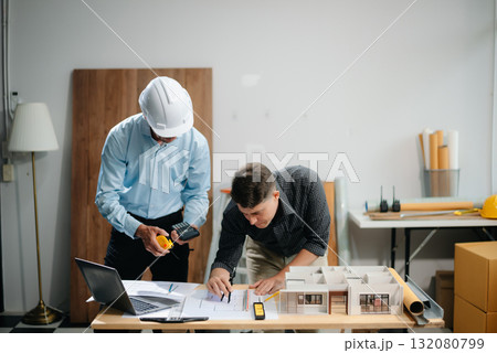 Contractor and architect looking at plan, tablet, laptop and talking about working on big project. Contractor and architect looking at plan, tablet, laptop and talking about working on big project. 132080799