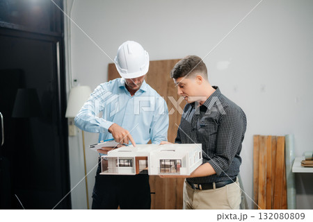 Professional collaboration in architecture. Two engineers work on construction plans, using tools like laptops, tablets, and scale models. Professional collaboration in architecture. Two engineers work on construction plans, using tools like laptops, tablets, and scale models. 132080809