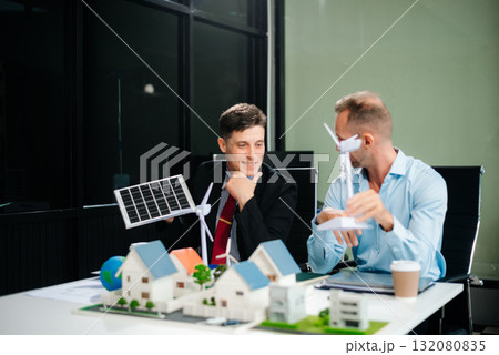 Experts collaborate on renewable energy solutions with house models, wind turbines, and solar panels, emphasizing green design Experts collaborate on renewable energy solutions with house models, wind turbines, and solar panels, emphasizing green design 132080835