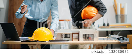 Professional collaboration in architecture. Two engineers work on construction plans, using tools like laptops, tablets, and scale models. Professional collaboration in architecture. Two engineers work on construction plans, using tools like laptops, tablets, and scale models. 132080982