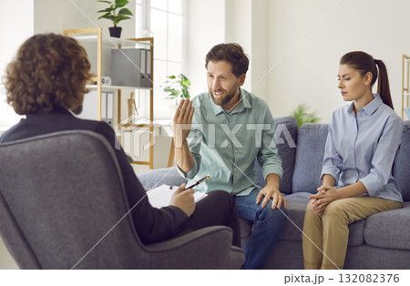 Young couple sitting on sofa and talking with psychologist on therapy session. 132082376