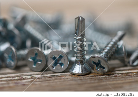 Pile of metal roofing screws on rustic wooden surface 132083285