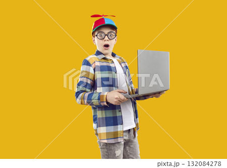 Surprised boy in funny glasses and colored cap with propeller looks directly into the camera, dressed in plaid shirt and gray jeans. Surprised boy in funny glasses and colored cap with propeller looks directly into the camera, dressed in plaid shirt and gray jeans. 132084278