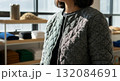 Asian woman wearing grey cable knit cardigan sweater standing in modern kitchen with wooden shelves and storage containers 132084691
