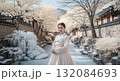 Beautiful young Asian woman in traditional Korean hanbok dress standing in snowy winter courtyard of historic Korean palace with icicles and frost covered trees 132084693