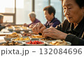 Elderly Asian woman carefully selecting and arranging colorful dried fruits nuts and traditional ingredients in small ceramic bowls on wooden kitchen counter with soft natural window lighting 132084696