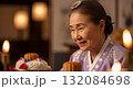 Elderly Korean woman in traditional lavender hanbok with floral patterns smiling warmly beside ceremonial food and candles during cultural celebration 132084698
