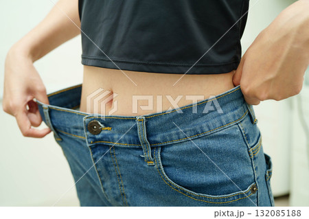 Young Asian woman losing weight wearing loose pants in oversize jeans. Young Asian woman losing weight wearing loose pants in oversize jeans. 132085188