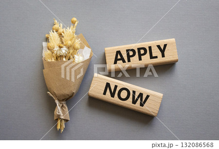 Apply now symbol. Concept word Apply now on wooden blocks. Beautiful grey background with bouquet of flowers. Business and Apply now concept. Copy space 132086568