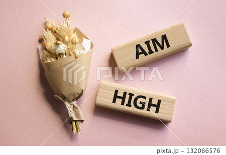 Aim High symbol. Wooden blocks with words Aim High. Beautiful pink background with bouquet of flowers. Business and Aim High concept. Copy space. 132086576